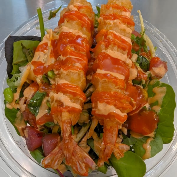 Two crispy tempura shrimp with spicy mayo and sriracha drizzle on a fresh poke bowl.