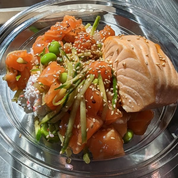 Poke Pub's salmon poke bowl with edamame, cucumber, and sesame seeds in a clear container.