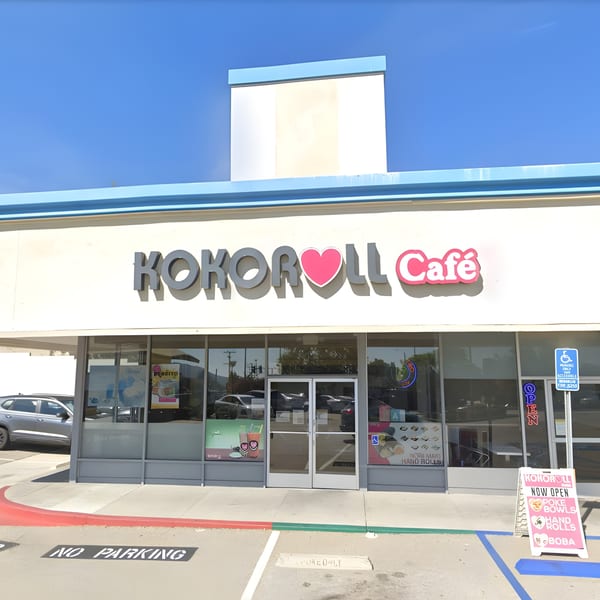 The exterior of Kokoroll Cafe, a poke restaurant, with a pink "Now Open" sign outside.
